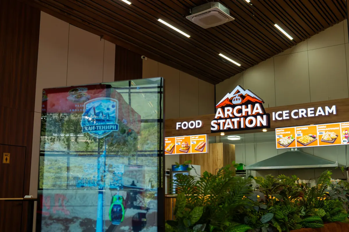 «Archa Station» фудкорту: тамак жана балмуздак жазуулары, өсүмдүктөр жана санариптик экран, жыгач шып.