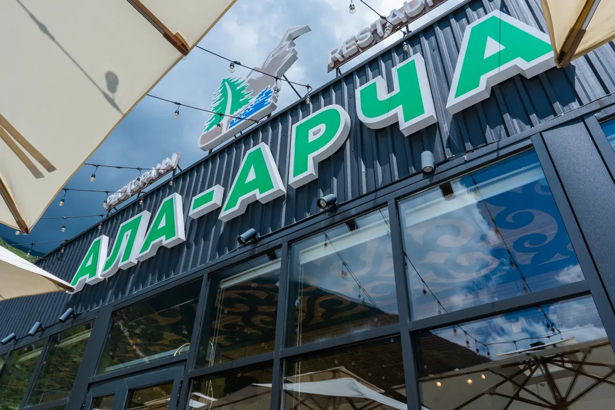 Ресторандын кара айнек имаратындагы жашыл «Ала-Арча» жазуусу, кол чатырдын четинен ылдыйдан тартылган.