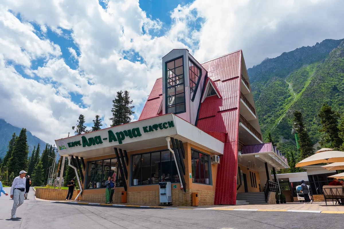 The red-roofed “Ala-Archa” building: the Ala-Archa café sign over the ground floor, balconies on the floors above, mountains behind.