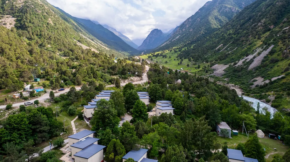 Aerial view of white cottages with blue roofs scattered among trees on the valley floor, the river and peaks beyond.