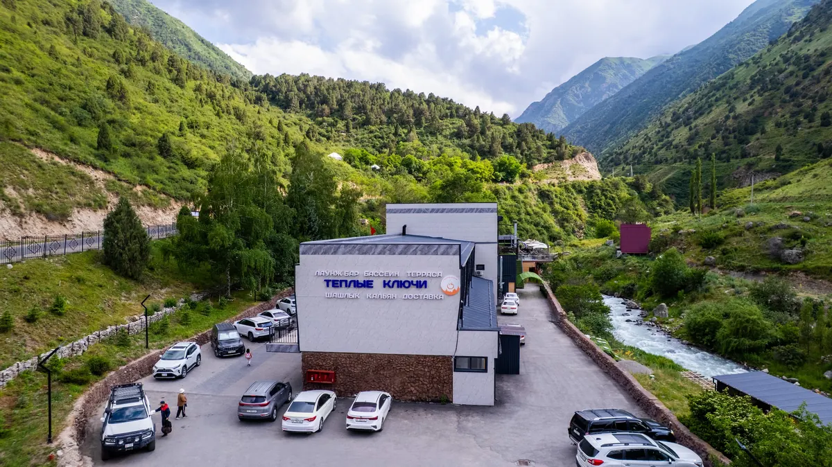 Aerial view of the "Теплые ключи" (Warm Springs) building with its car park, the river on the right and the valley behind.
